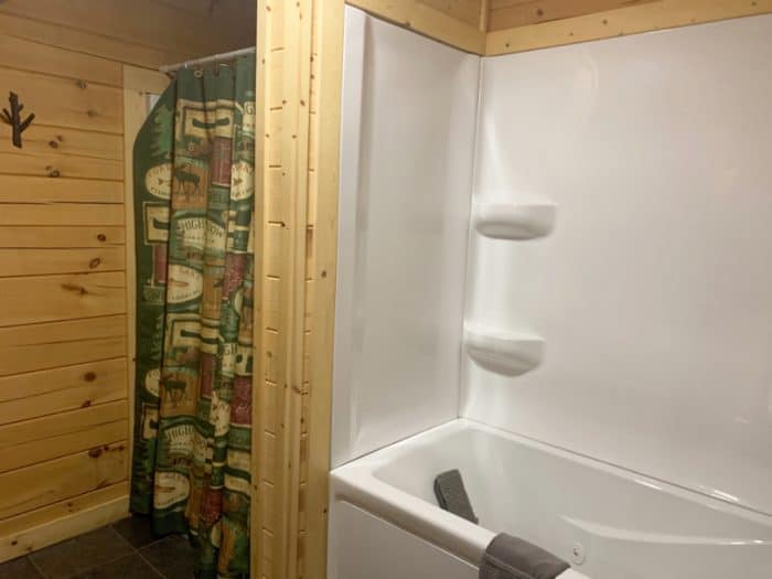 White bathtub on the right with a gray towel hanging over the edge and a green, beige and orange shower curtain on the left