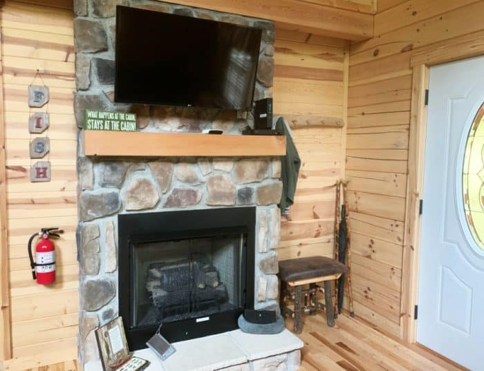 Stone fireplace against a wooden wall with a TV on top.