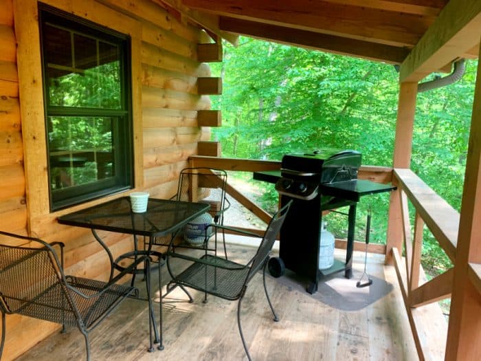 Log cabin outside porch with black grill and black wrought iron table with 3 chairs