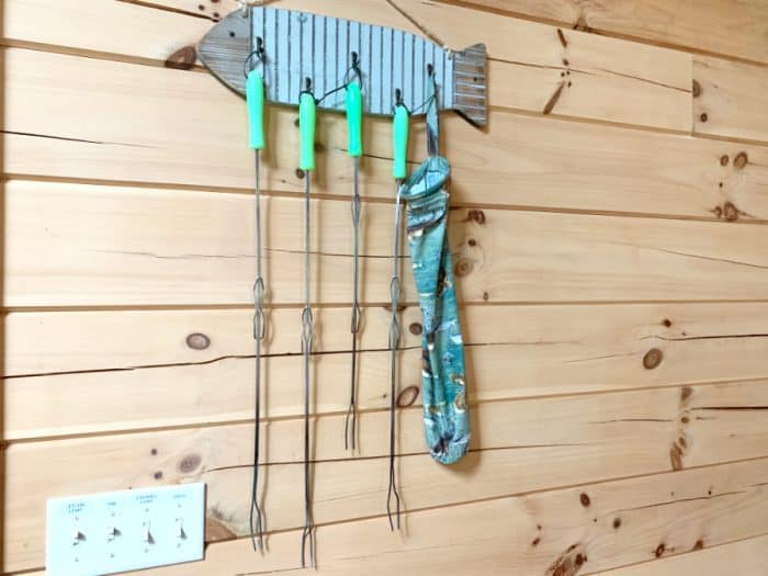 Light wooden wall with 4 metal campfire roasting sticks hanging on it.